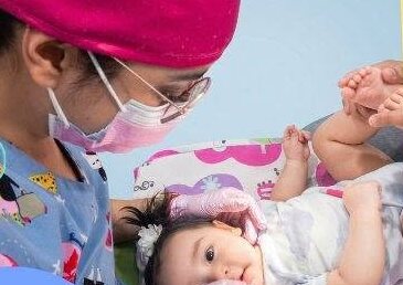 La Dra. Denisse Cortinas revisando la boca de una bebé recostada en el consultorio de DC Kids